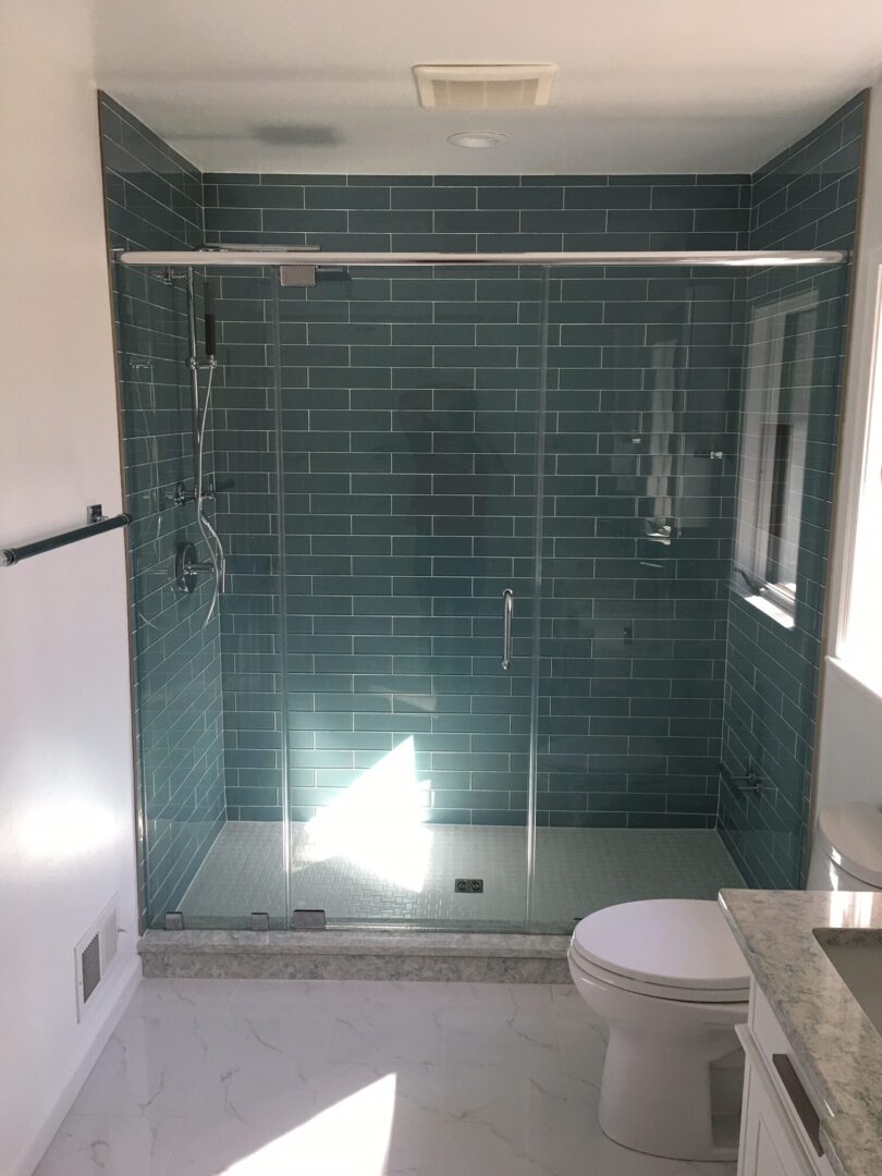 A bathroom with a glass shower door and tiled walls.