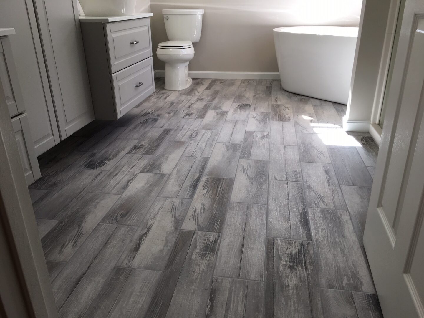 A bathroom with wood floors and white cabinets.